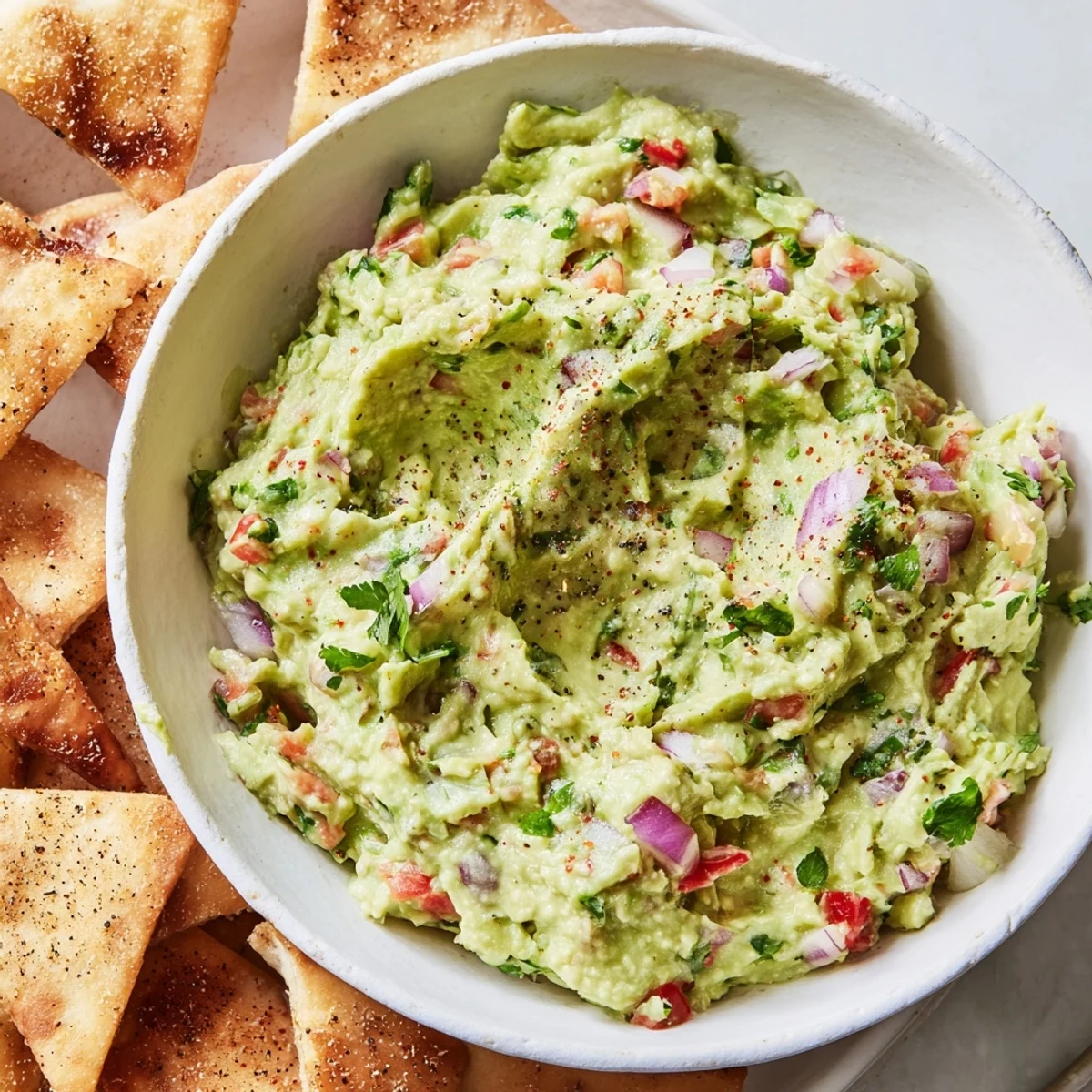 Freshly baked pita chips with a side of creamy guacamole, an easy American snack to make.