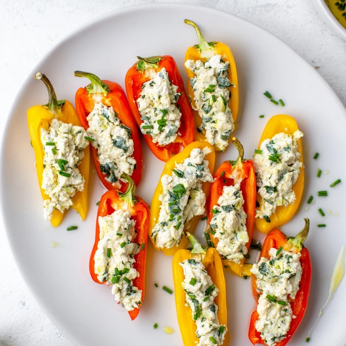 A platter of mini bell pepper halves with feta filling, drizzled with olive oil and chives for serving.