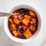 Close-up of colorful, steaming sweet potato & black bean chili with cilantro garnish.