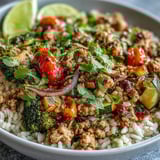 A vibrant bowl featuring seasoned ground turkey, caramelized roasted vegetables, and hearty quinoa, garnished with cilantro and lime.
