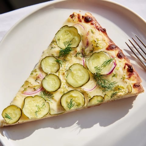 Crispy pickle pizza topped with creamy sauce and fresh dill garnish  