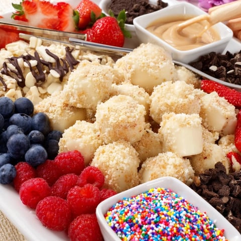 Deconstructed dessert board featuring creamy cheesecake bites and colorful toppings for customization.  