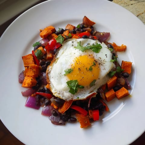 Golden brown Sweet Potato & Black Bean Breakfast Hash, topped with perfectly cooked sunny-side-up eggs.