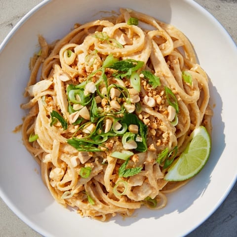 Steaming bowl of Thai Peanut Chicken Pasta, garnished with fresh herbs and peanuts, ready to eat.
