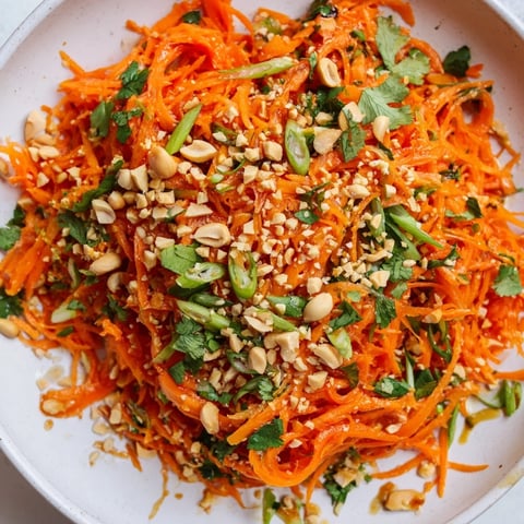 Vibrant Spicy Carrot Salad with shredded carrots, a fiery Asian-inspired dressing, and chopped peanuts.