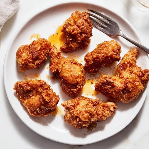 Crispy fried chicken thighs glistening with a sticky hot honey butter sauce, served on a platter with fresh parsley garnish.  