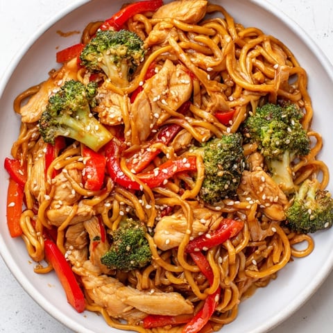 A vibrant bowl of Spicy Ramen Stir-Fry features glossy noodles tossed with tender chicken, crisp broccoli, and bell peppers in a fiery red sauce.  
