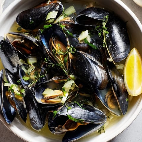Enjoy a steaming bowl of Belgian Moules Marinière, a classic dish with savory garlic and wine broth.