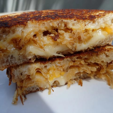 Golden, crunchy fried onions add texture to a Crispy Onion Grilled Cheese served warm beside creamy tomato soup.