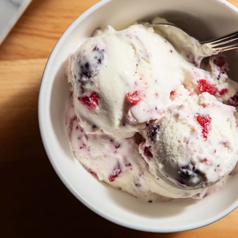 Scoops of creamy cottage cheese ice cream, with mixed berries shown on a white serving dish.