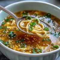 Silky egg ribbons swirl in a savory, aromatic broth with fresh scallions, creating a comforting homemade egg drop soup.  